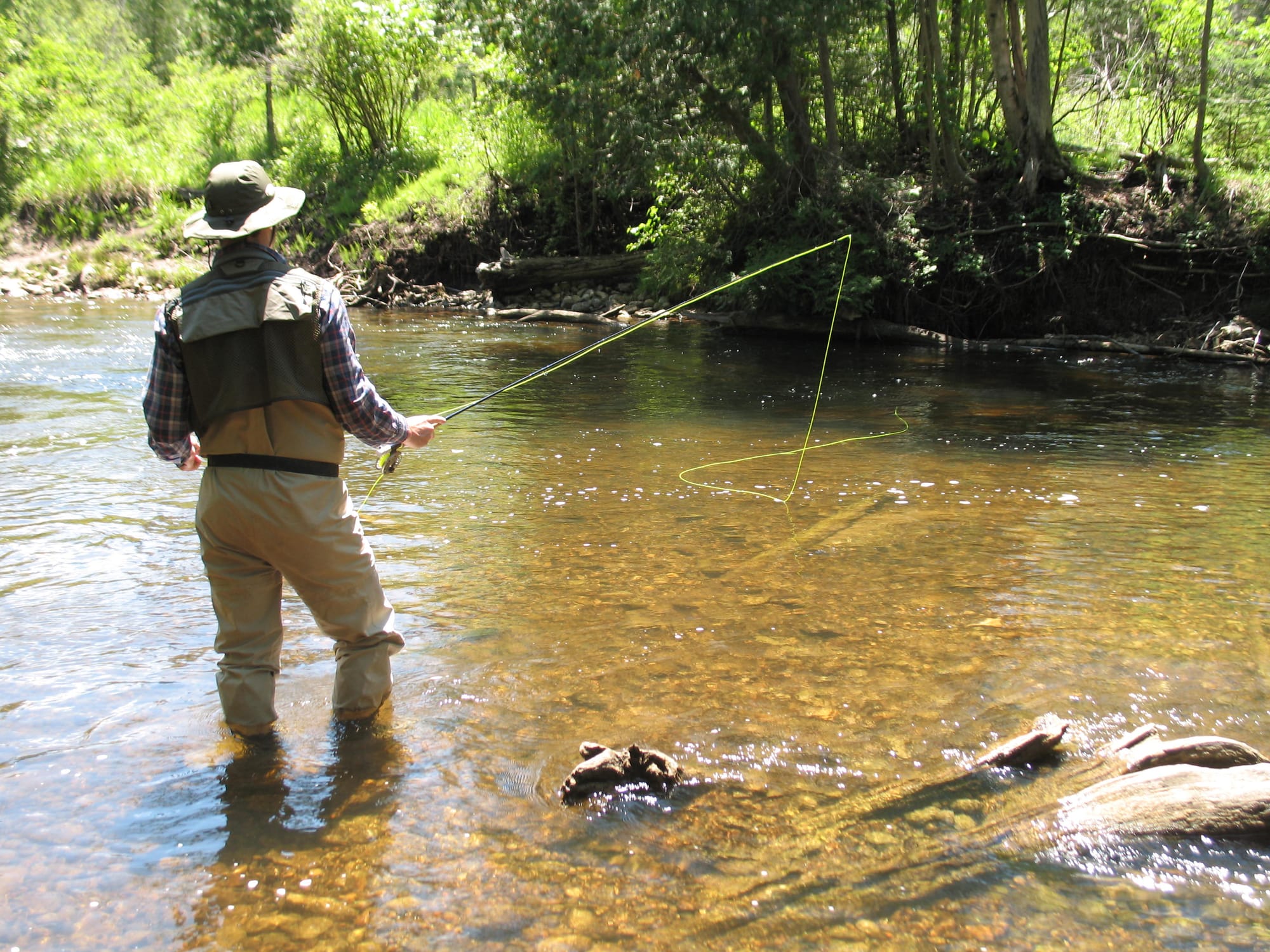 A fly angler watches his fly drift into some shadows down a shallow river