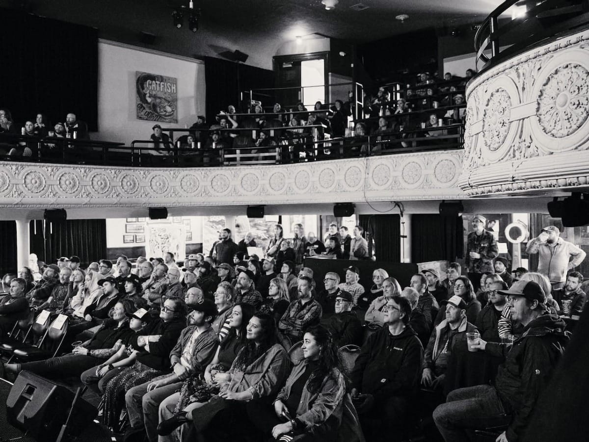 Black and white photo of crowded theater with ornate balcony, audience watching