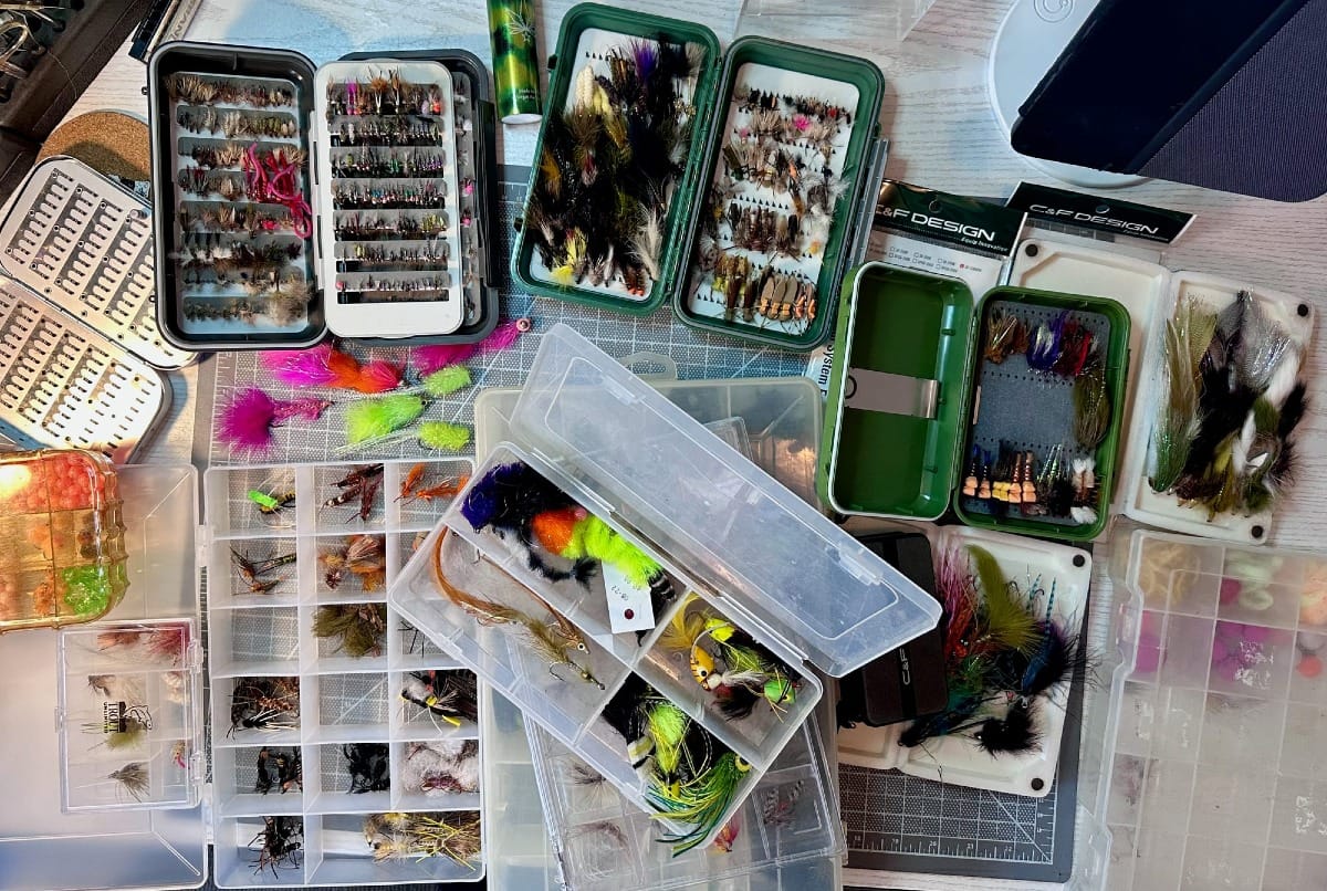 Fly tying table with open fly boxes displaying assorted flies, loose streamers, and organized storage containers
