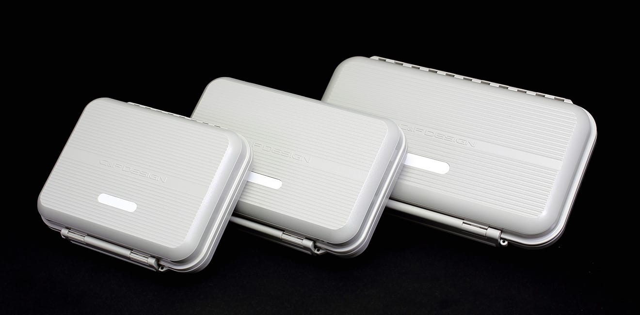 Three C&F Design fly boxes in white, graduated small to large, on black background
