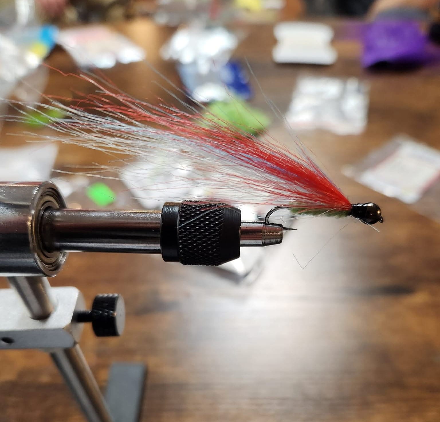 A streamer secured in a vise during a group fly tying session, with tying materials visible in the background.