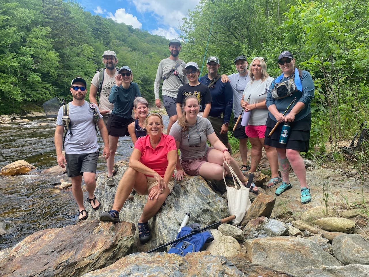 Group of twelve therapist trainees pose on riverside boulders with fly rods during a Seiyu Institute fly fishing program.