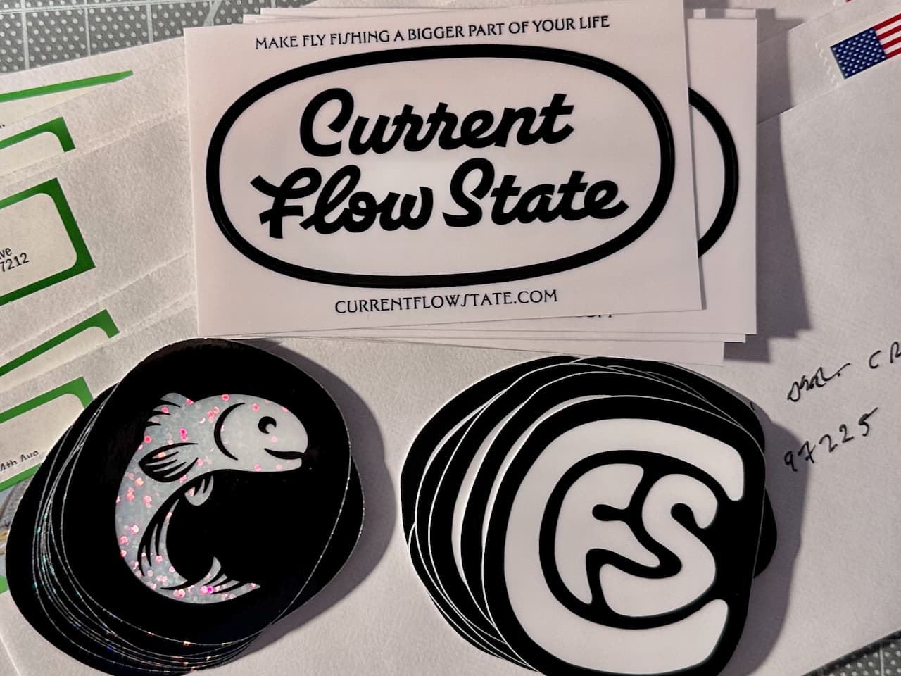 Three Current Flow State stickers, oval logo, holographic trout, and CFS monogram, fanned out on envelopes ready to mail.
