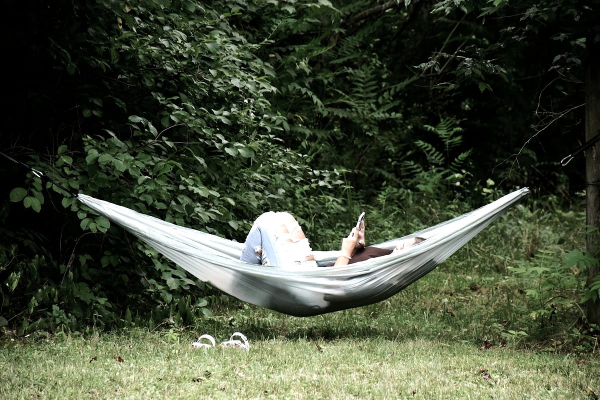 A person in jeans swings in a hammock while looking at their phone