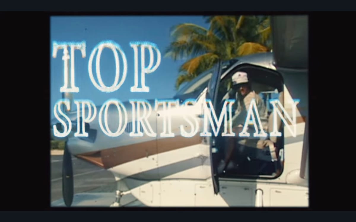 A screenshot from a vintage-looking airplane shows a man leaning out of a small airplane, with the title lettering TOP SPORTSMAN superimposed