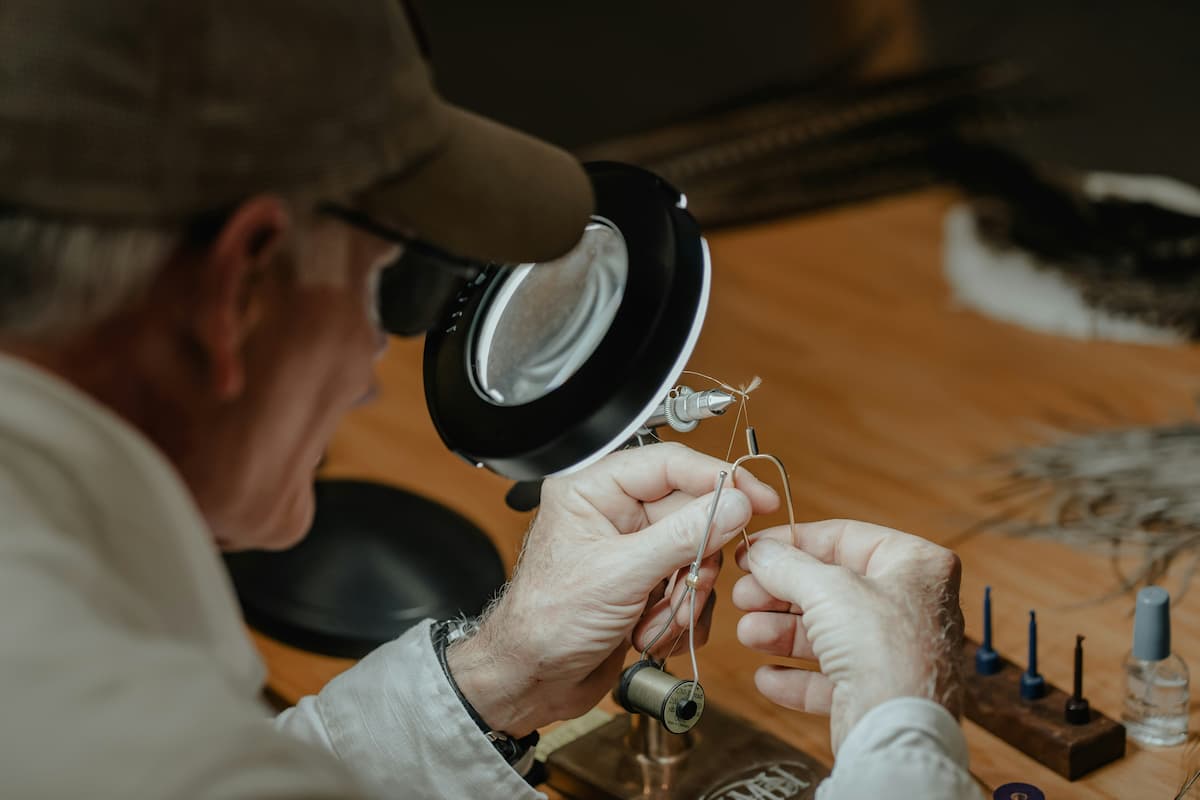 A fly tier works under a magnifying lens, threading a hook with the close concentration the craft demands.