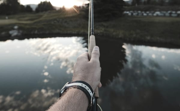 A hand holding a fly rod at a pond is ready to set the hook when the indicator moves