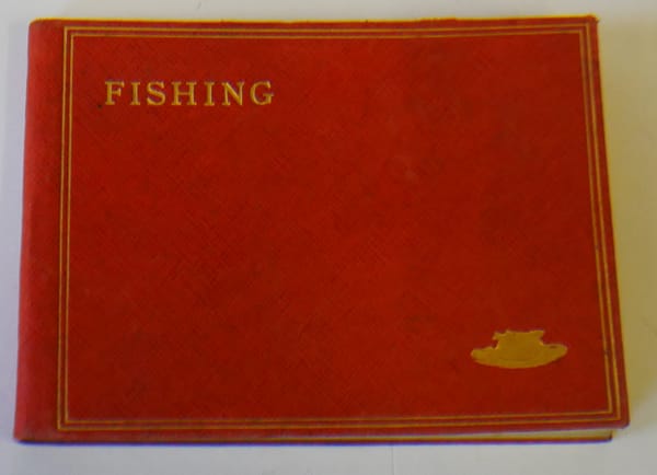 An old red fishing logbook has FISHING gold-embossed in the upper left corner, and some sort of fish-related icon, a creel maybe, in the lower right.