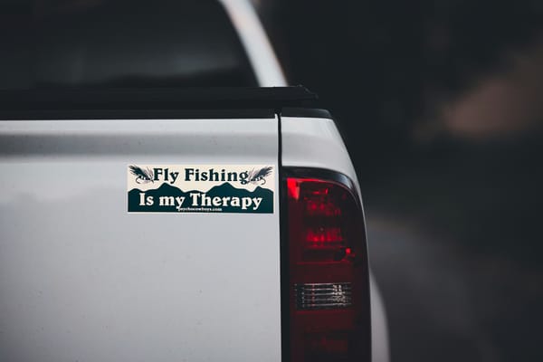 "Fly Fishing Is my Therapy" bumper sticker with wet fly illustrations and mountain silhouette on the tailgate of a white pickup truck.