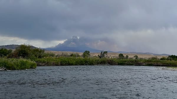 A fire burns on a butte in the background of the Madison River in Montana